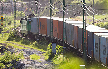 Godståg med containrar i vårgrönt landskap.