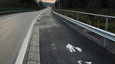 Foto från nya cykelbanan som löper längs en bilväg, skog på båda sidor