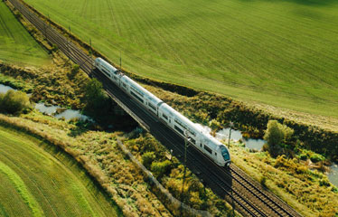 Flygfoto av ett tåg ute på järnvägen i grönt åkerlandskap. 