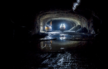 En mörk tunel. I slutet av tunneln lyser två gula arbetsfordon upp utrymmet.