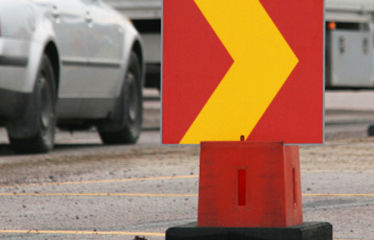 Närbild på en röd och gul vägskylt som pekar ut körbanan vid en trafikomläggning.