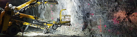 Ett gult arbetsfordon med armar framtill står framför en tunnelvägg.