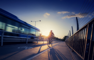 Cyklist och buss på bro i motljus