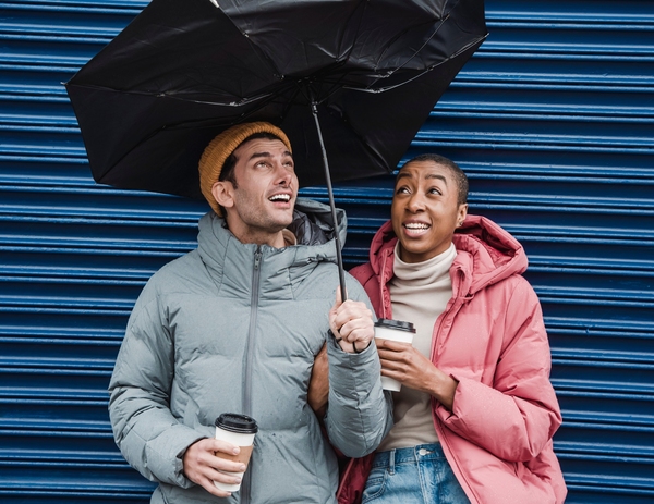 Två personer ler och håller ett paraply tillsammans framför en blå bakgrund. Foto: Klaus Nielsen, Pexels