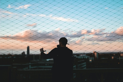 Person som betraktar solnedgången genom ett nätstängsel. Foto: TomSodoge/Unsplash