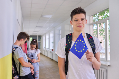 Tonåring i skolkorridor håller en EU-flagga, andra studenter i bakgrunden. Foto: VH-STUDIO/mostphotos.com