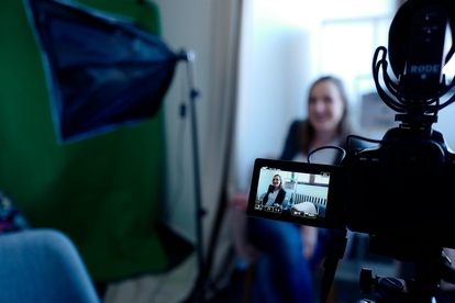 Person sitter och ler under en videoproduktion, synlig genom en kameradisplay. Foto: Cowomen/Pexels