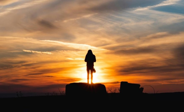 Silhuett av en person stående på en klippa mot en solnedgång. Foto: Tothszabolcs/Pexels
