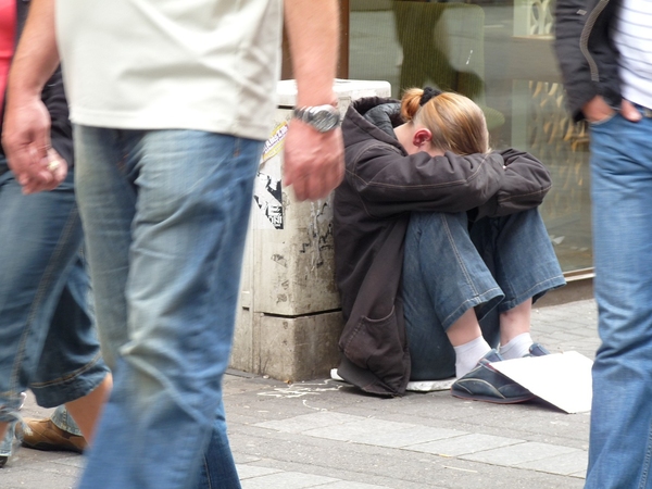 Person sitter nedkurad på gatan medan människor går förbi. Foto: Jackie Chance