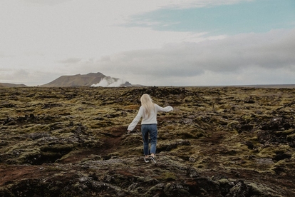 Person med utsträckta armar på lavafält med berg i bakgrunden. Foto: Alleksana/Pexels.com