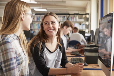 Två studenter arbetar tillsammans vid en dator i ett bibliotek. Foto: Mostphotos