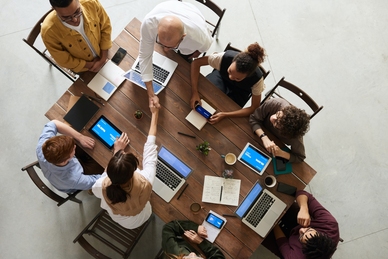 Grupp av personer som arbetar tillsammans runt ett bord med bärbara datorer och dokument. Foto:Fauxels/Pexels