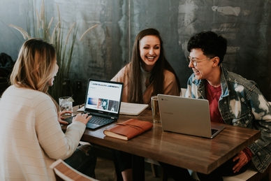 Tre personer sitter och skrattar vid ett bord med laptops. Foto: Unsplash