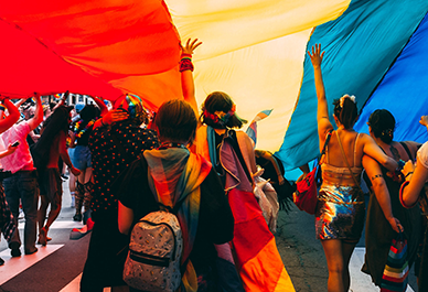 Människor som deltar i en prideparad och håller i en stor regnbågsflagga.
