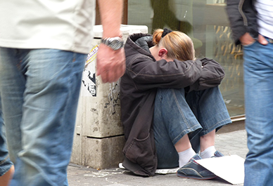 Person sittande på trottoaren med huvudet vilande på knäna.