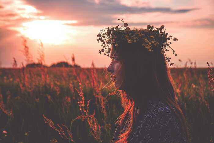 Ung person med blomsterkrans i håret i solnedgången över ett fält. Foto: Unsplash