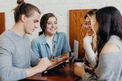 Fyra unga personer sitter och samtalar vid ett bord med mobil och kaffekoppar. Foto: Unsplash