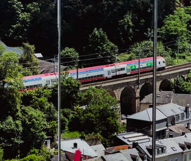 Tåg passerar över en stenbro bland gröna träd.