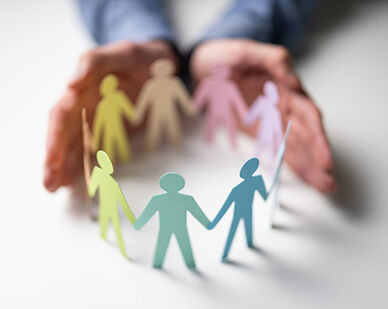 Händer som omsluter en cirkel av pappersfigurer i olika färger som håller varandra i händerna.