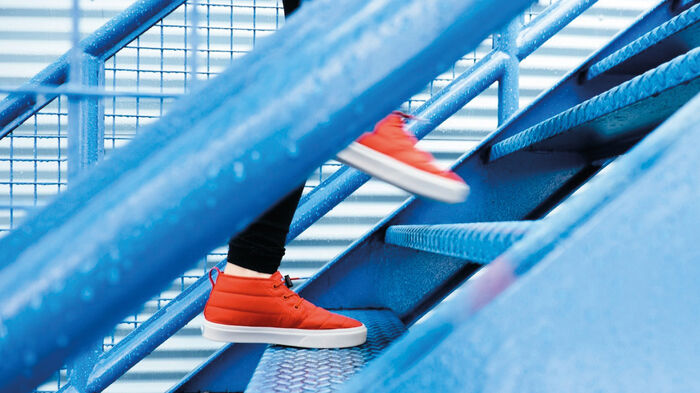 Person i röda skor går upp för en blå trappa. Person i röda skor går upp för en blå trappa.