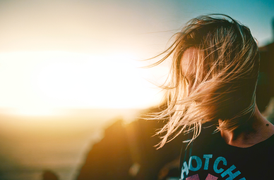 Person med hår som blåser i vinden vid solnedgång över kusten