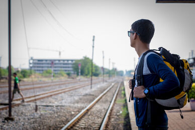 Person med ryggsäck står på perrong och tittar längs tågspåren.