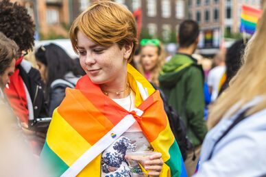 Ung person med regnbågsflagga runt axlarna i folkmassa
