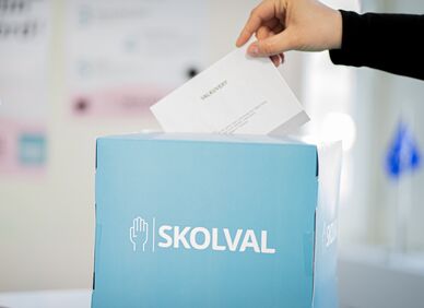 Hand som lägger en röstsedel i en blå vallåda märkt "SKOLVAL".