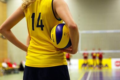 Volleybollspelare med nummer 14 håller bollen vid sidan av på en inomhusplan, lagkamrater i bakgrunden