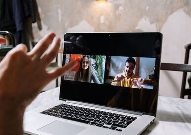 Person gestikulerar vid bärbar dator som visar två personer i videosamtal. Foto: Pexels.com/cottonbro studio
