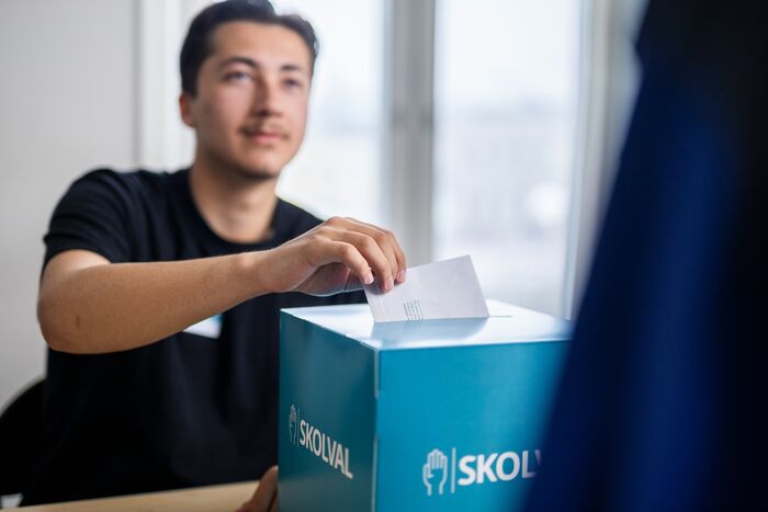 Person som lägger en röstsedel i en valurna märkt "Skolval". Person som lägger en röstsedel i en valurna märkt "Skolval".