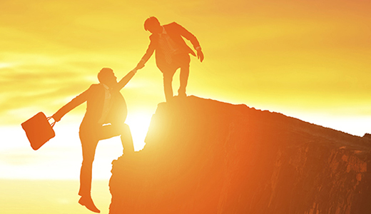 Temabild på en person som hjälper en annan person upp på en bergstopp.