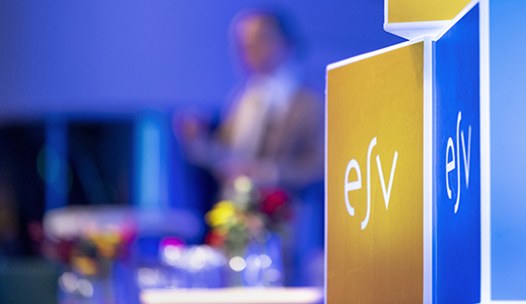 Person talar i balgrunden framför ljuskuber med ESV:s logotyp.