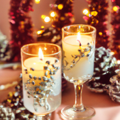 Två tända ljus i dekorativa glas med juldekorationer i bakgrunden.