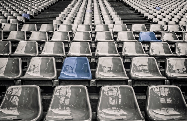 Tomma gråa stolar på en idrottsstadion, några enstaka stolar är målade blåa.