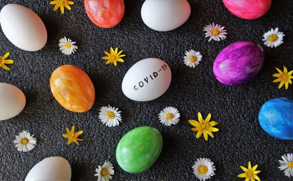 Ägg målade i olika färger bland blommor, ett ägg har texten covid-19.