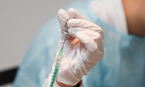 En hand med skyddshandske på håller på att fylla en spruta med vaccin.