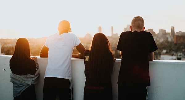 Foto: Devin Avery, Unsplash. Fyra ungdomar står med ryggen mot fotografen och tittar ut över en storstadsvy.
