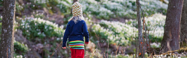 Ett barn i färgglada kläder som utforskar en skog med vårblommor.