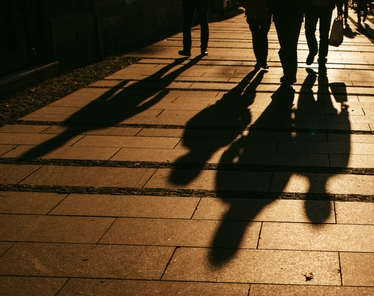 Personer som går på en stadsgata med sina långa skuggor sträckande sig i solnedgången.