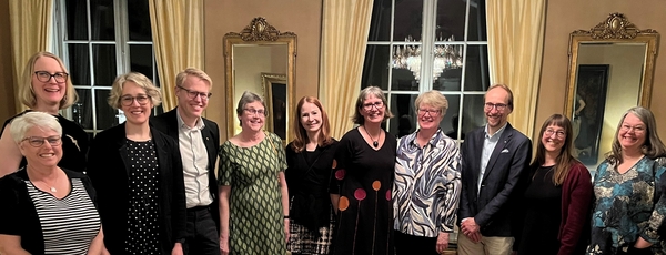 Grupp av leende människor poserar i en elegant salong med speglar och gyllene ramar.
