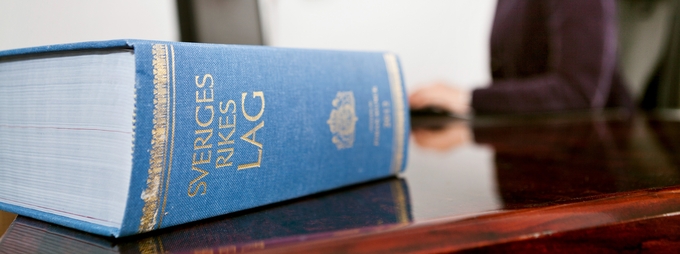 Blå lagbok "Sveriges rikes lag" på skrivbord med suddig person i bakgrunden.