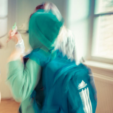Ett suddigt barn med turkos hoodie och ryggsäck som går förbi ett fönster inomhus