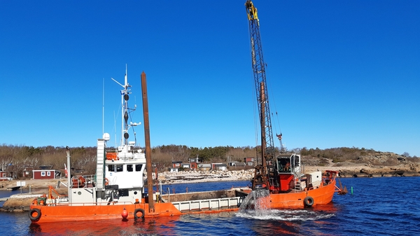 Två orange arbetsbåtar vid kusten som utför grävmuddring.