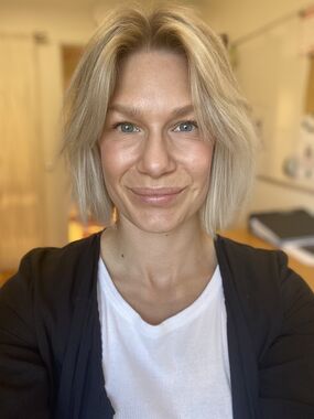 Närbild på en leende kvinna med kort blont hår i inomhusmiljö.