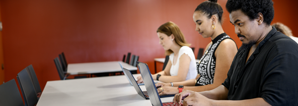 Studenter som arbetar koncentrerat med sina laptops i ett klassrum.