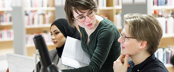 Studenter och lärare diskuterar ett projekt i biblioteket.