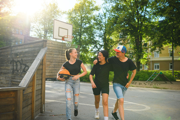 Tre ungdomar som går över en basketplan