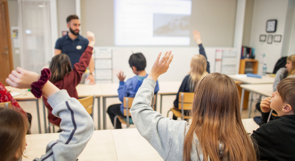 Ett klassrum med elever som räcker upp händer.