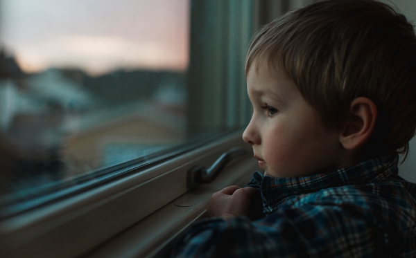 Pojke tittar ut genom fönster i kvällsljus.